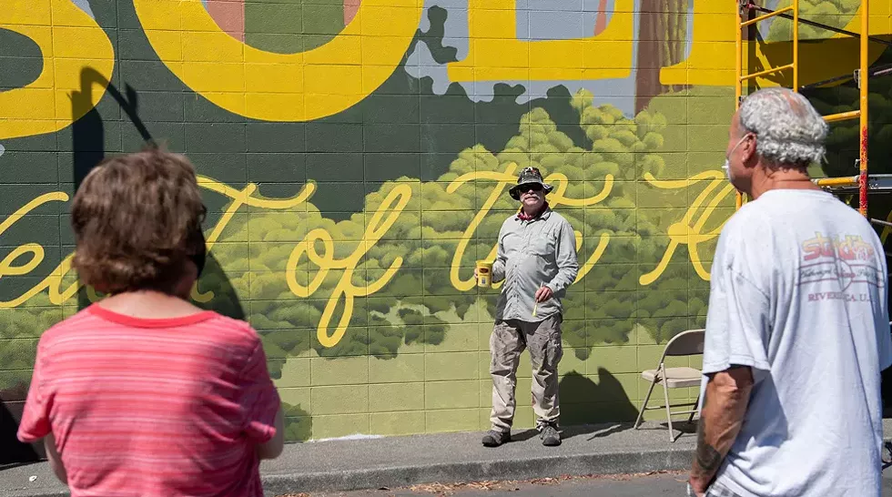 Local copper artist Scott Hemphill talks with a couple taking in the murals during the festival. Hemphill was helping with the lettering on Ellie Gainey's mural "Heart of the Redwoods," located on the side of the Toy Box. It was the largest mural of this year's festival. - PHOTO BY MARK MCKENNA