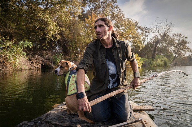 Josh Lowe, 32, made a makeshift raft out of longboards and wood to get across the San Mateo Creek to where he has been staying in San Clemente on Nov. 6, 2021. Lowe moved to the woods with his dog Anna since the encampment on the CalTrans property was disbanded on August 27th. - PHOTO BY ARIANA DREHSLER FOR CALMATTERS