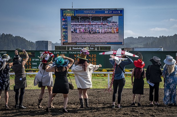 The Ladies Hat Day contenders catch themselves on the screen at the racetrack. - PHOTO BY MARK LARSON