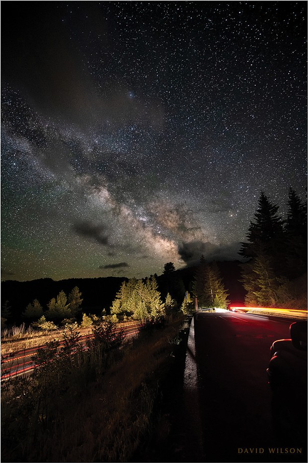 With the grand Milky Way soaring overhead, streaking car lights in the southbound lanes of U.S. Highway 101, paralleling the Eel River valley, converge with the brighter streaks of a car leaving the Vista Point south of Stafford, Humboldt County. June 9, 2021.