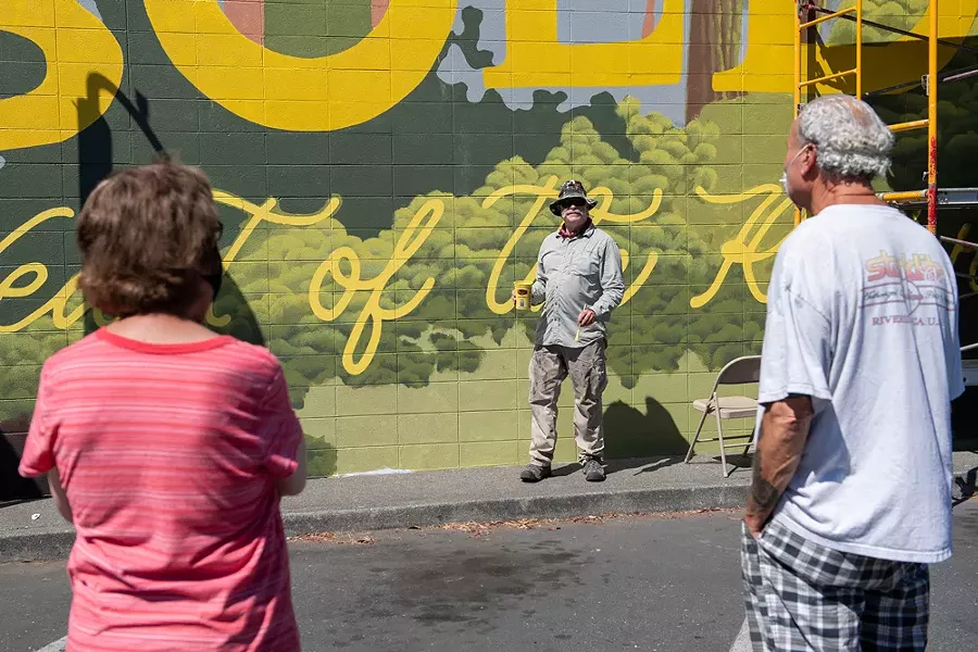 Local copper artist Scott Hemphill talks with a couple taking in the murals during the festival. Hemphill was helping with the lettering on Ellie Gainey's mural "Heart of the Redwoods," located on the side of the Toy Box. It was the largest mural of this year's festival. - PHOTO BY MARK MCKENNA