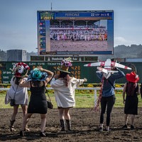 The Ladies Hat Day contenders catch themselves on the screen at the racetrack.