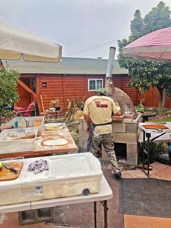 BEHIND THE SCENES Kean McCabe, the chef behind Earth and Oven, checks on a pizza order in his self-constructed wood-fired oven. - PHOTO BY MALEA MARTIN