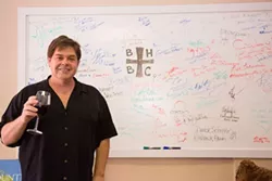 LEAVING THEIR MARK: Local chefs, winemakers, beer brewers, cookbook authors, business owners, and general wine lovers sign their names on David Wilson’s famous white board, located within his Grape Encounters Radio Studio in Atascadero. - PHOTO BY TOM FALCONER