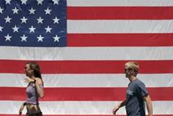 YOUNG AMERICANS : A young couple passes a huge flag on their way to the parade. - PHOTO BY GLEN STARKEY