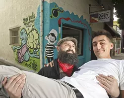 A TRICKY ANGLE? : San Luis Art Supply owner Neal Breton (bearded, left) hired graffiti artists Nic Rodriguez (not pictured) and Julian Small Calvillo (cradled in Breton’s arms) to paint a mural outside his shop. - PHOTO BY STEVE E. MILLER