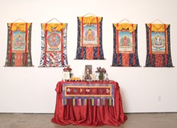 DEITIES BY THE HANDFUL :  Five thankas from the exhibit, depicting five different Buddhas or deities, are mounted on silk brocade backgrounds. The center column beneath the image represents a door through which people can enter the thanka. - PHOTO BY STEVE E. MILLER