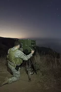EYES ON THE WATER : A National Guard soldier peers through a LRAS-3 long-range night vision scope to scan the horizon for suspicious watercraft. The U.S. National Guard’s counter-drug coastal surveillance team took New Times for a ride-along atop the hills overlooking the Ventura County coastline. - PHOTOS BY STEVE E. MILLER