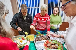FEAST TIME: Jamie, Betsy, and Willow Bettencourt (left to right) volunteer as a family, serving food at a community dinner at the Vets Hall in Morro Bay the week of Christmas. - PHOTO BY JAYSON MELLOM