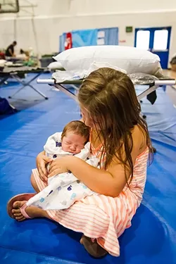 FIRST FIRE: Unofficially the youngest refugee of the Chimney Fire, 6-day-old Xander Earl sleeps in the arms of his half-sister Lexi Leberett, 5, at the Red Cross Shelter in the gym of a Paso middle school on Aug. 23. Their mother, Roxanne Howard, arrived home from the hospital on Saturday, Aug. 20, just 20 minutes before the family had to evacuate from the fire. - PHOTO BY JAYSON MELLOM