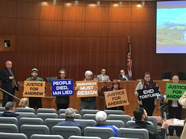 About 15 demonstrators stood silently while one lay in a stretcher in front of the SLO County Board of Supervisors on March 20, in protest of former Atascadero resident Andrew Holland's death in the county jail. Board Chairman John Peschong (left) looked on after calling a ten minute recess. - PHOTOS BY PETER JOHNSON