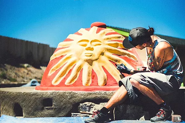 ARTISTIC LICENSE Chad Franco, who recently started a cob building business called Cobber's Delight, uses iron oxides mixed with lime wash to paint the lime plaster covering a cob pizza oven he built in a client's backyard. Find more of his work on Instagram @CobbersDelight. - PHOTO BY BRANDI LOPEZ PHOTOGRAPHY