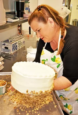 DRESS IT UP Taco Temple pastry chef Nicole DeWolf packs chopped walnuts onto the bottom of a freshly frosted carrot cake. - PHOTOS BY CAMILLIA LANHAM