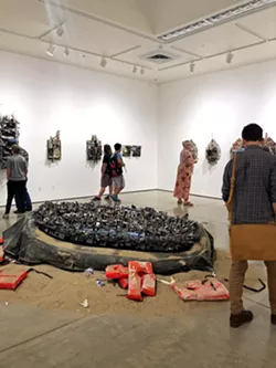 CENTERPIECE Hafez's sculptural installation titled Desperate Cargo sits in the middle of the Miossi Gallery, as gallerygoers peruse the exhibit on its opening night. - PHOTO BY MALEA MARTIN