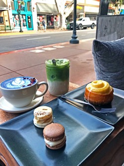 PRIME WINDOW SEAT One of the best seats in the house at Kin is a Moroccan-style window nook, perfectly designed for people watching. Pictured is the Butterfly Pea Latte, iced Amethyst Matcha, with Buttercup Bakery chocolate-vanilla and pecan praline macarons and warmed orange cardamom roll. - PHOTO BY BETH GIUFFRE