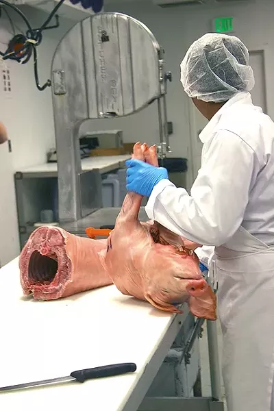 ALL IN THE WRIST: A commercial slicer, manned by a professional butcher, slices up a whole hog at J&R Meats in Paso Robles. - PHOTO BY REID CAIN