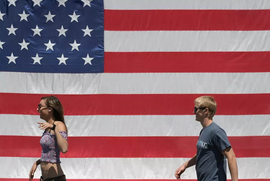 YOUNG AMERICANS : A young couple passes a huge flag on their way to the parade. - PHOTO BY GLEN STARKEY