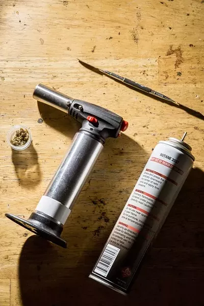 AN EXPLOSIVE TREND: All the makings for smoking concentrated cannabis (minus the bong), and a can of butane. Using specialized implements that attach to bongs, a metal piece is heating with a torch, and then a dab is placed on the metal, causing it to burn. - PHOTO BY HENRY BRUINGTON