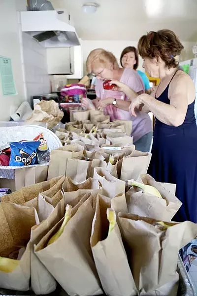 PEOPLE’S KITCHEN: Volunteers Debbie, Clara, and Mary (left to right) prepare paper bag dinners at Second Baptist Church in Paso Robles for locals in need. The People’s Kitchen is able to serve dinners Monday through Friday because of the efforts of faith-based organizations. - PHOTO BY DYLAN HONEA-BAUMANN