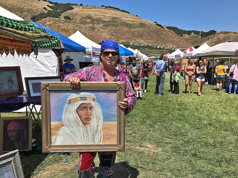 DRESSED TO CHILL Artist E.T. McSparron holds up one of his paintings at Art in the Park. - PHOTOS BY TREVER DIAS