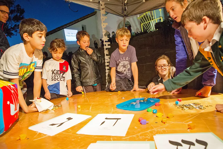 SPIN Kids gather around a table to spin the dreidel in Mission Plaza. The Jewish Community Center of SLO invites the public to participate in Hanukkah festivities like this on Dec. 2. - PHOTOS COURTESY OF THE JCC OF SLO