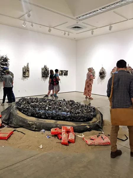 CENTERPIECE Hafez's sculptural installation titled Desperate Cargo sits in the middle of the Miossi Gallery, as gallerygoers peruse the exhibit on its opening night. - PHOTO BY MALEA MARTIN