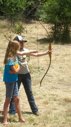 TAKE AIM : A Camp Natoma regular helped a younger girl take her first shot with a bow and arrow. The camp provides weeklong, overnight retreats that include swimming, crafts, and archery for kids ages 6 to 17. - PHOTO BY NICK POWELL