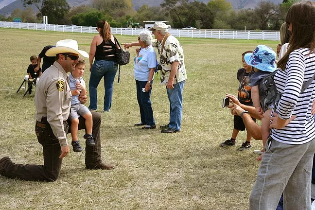 GOOD GUY WITH A GUN: SLO County Sheriff Ian Parkinson takes a knee for a photo op with a young admirer. - PHOTO BY GLEN STARKEY