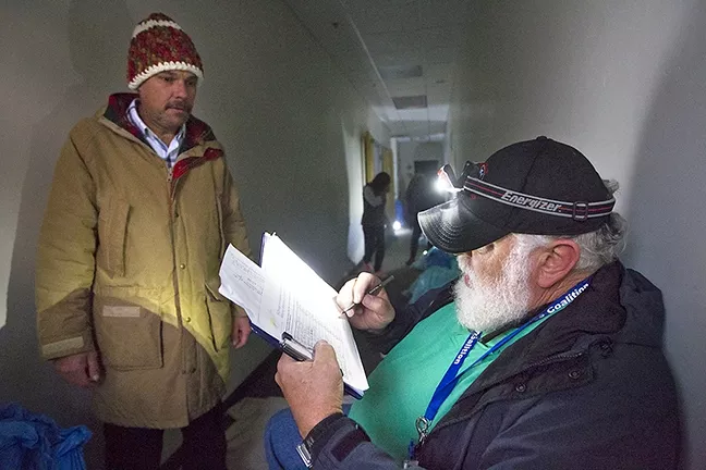 PERSON-TO-PERSON: Volunteer Jeff MetCalfe checks Dave Trout into the emergency homeless shelter on Feb. 17 using a headlamp because the power’s out. “This is citizen-to-citizen,” MetCalfe says of the coalition’s work. “I’m happy here.” - PHOTO BY JAYSON MELLOM