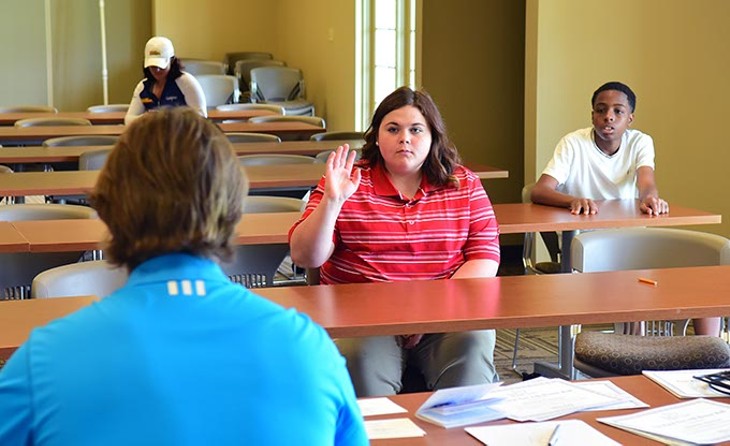 Kirstin Westlake raisers her hand to answer a question during a short classroom session with director Dustin Semsch and others in her age group before the young golfers hit the course on a recent Saturday.  mh