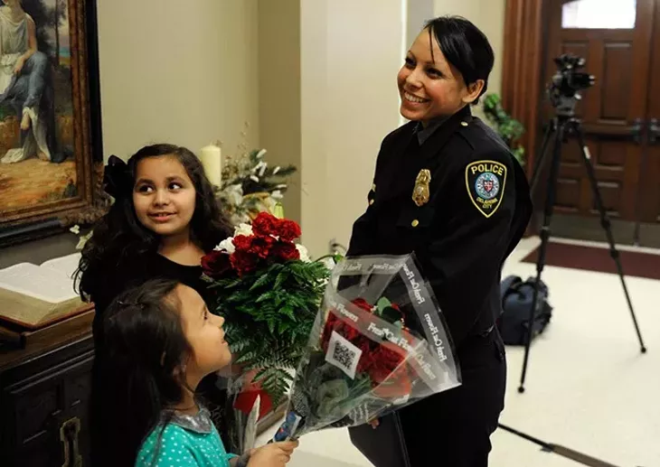 Alma Deloera recieves flowers from her daughter, Tatiana, 7, and her niece, Belle Reyna, 6, after the Oklahoma City Police Academy Recruit Class 132 graduation at First United Methodist Church, Thursday, Dec. 4, 2014. - GARETT FISBECK