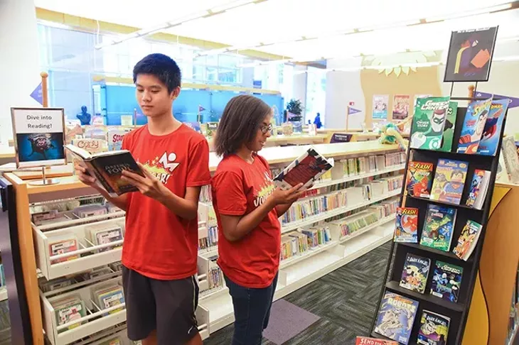 Alberto Liu and Jessica Jones, volunteers with the Summer Reading Program, help young readers get signed up, in the Ronald J. Norick Downtown Library. mh