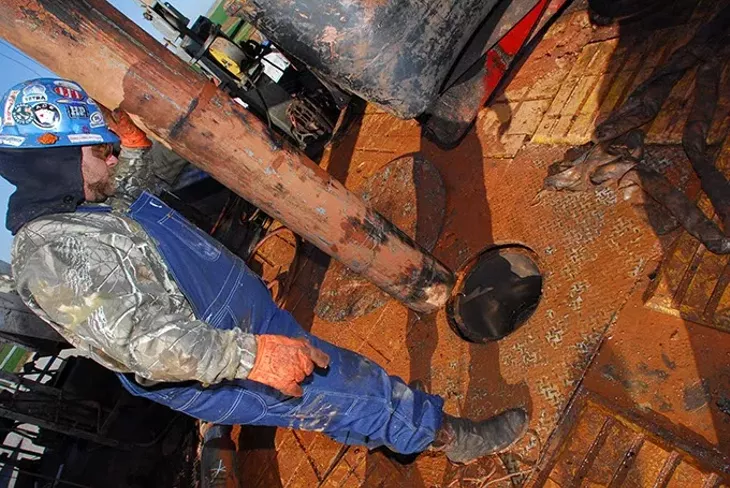 Jason Roberts, "Driller" on a Devon natural gas drilling rig in the CANA field near Calumet Oklahoma, looks down through the drilling deck, preparing to guide a tool through. mh