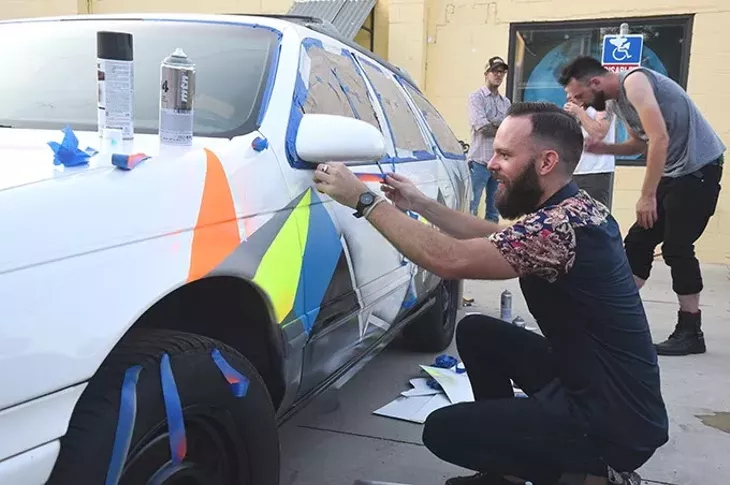 Jerrod Smith, owner of The Society collective art studio, puts a paintjob on a old Ford stationwagon, with help from fellow collective artists as part of the 4 year celebration at and in the parking lot of the art space in the Plaza District, 8-14-15. mh