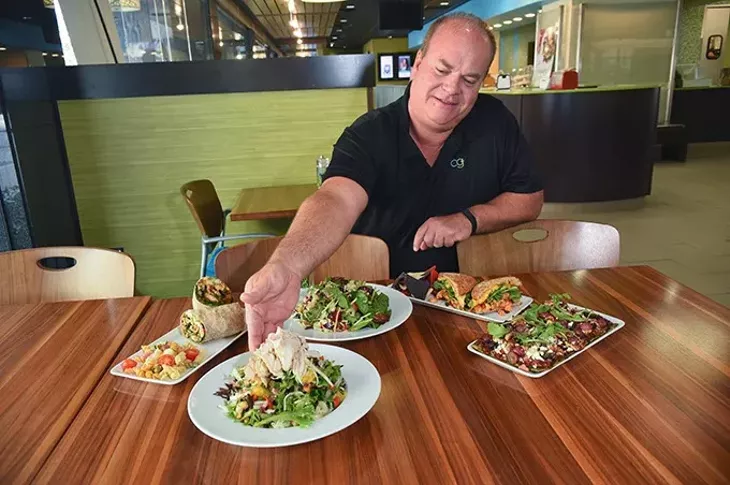 Owner Scooter Aselton with new and seasonal menu Items, from left, Southwest Spicy Wrap, Lemon Lychee Chicken Salad, the seasonal Summer Berry Salad, Sriracha Chicken Sandwich, and one of his favorites, the new Plaza Skinny Flatbread, at the Downtown OKC Coolgreens, 9-11-15. - MARK HANCOCK