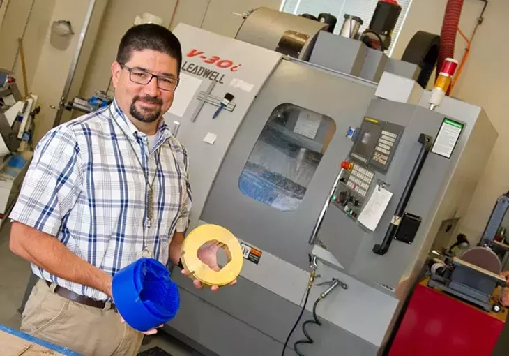 Senior Machinist at ProCure, Dirk Ramsey creates custom patient devices for proton therapy. Photo/Shannon Cornman - The blue device on the left is a computerized image of the patients tumor called the compensator, that guides the laser in the proper path so surrounding tissue won't be disturbed. The brass device on the right is another shape of the patient's tumor called the aperture that fits between the compensator and proton machine. The Leadwell V-30i, highly sophisticated computerized machine in the background is molding the devices. Photo/Shannon Cornman - SHANNON CORNMAN