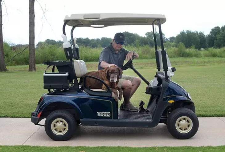 Scout rides on a golf cart with Chris Chesser, golf course director, at Firelake Golf Course in Shawnee. - GARETT FISBECK