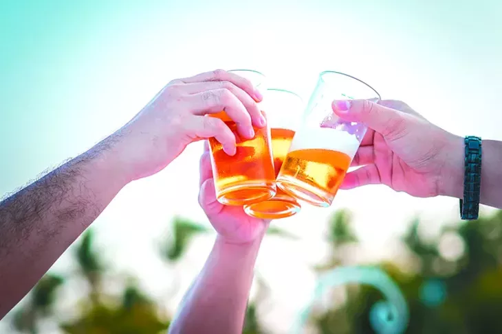 Hand holding glasses of beer clinking together at outdoor - BIGSTOCK