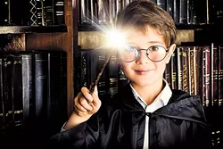 A boy stands with magic wand in the library by the bookshelves with many old books. Fairy tales. Vintage style. - BIGSTOCK