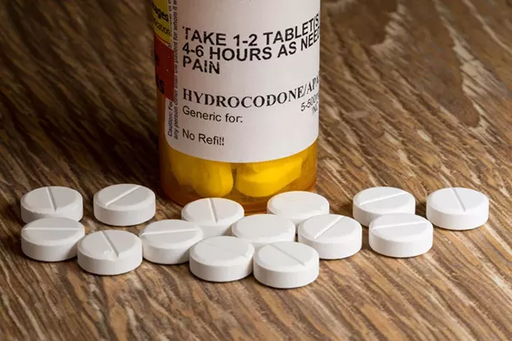Close photo of prescription bottle for Hydrocodone tablets and pills on wooden table for opioid epidemic illustration - BIGSTOCK