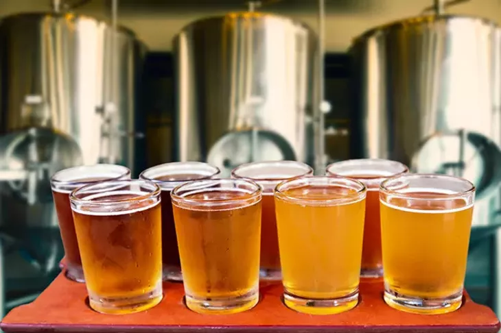Beer flight of eight glasses of craft beer on a serving board with fermenting tanks background. - ** Note: Shallow depth of field - BIGSTOCK