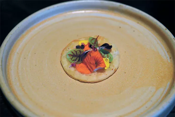 A pork heart “cracker” topped with yogurt, red bell pepper and flower petals