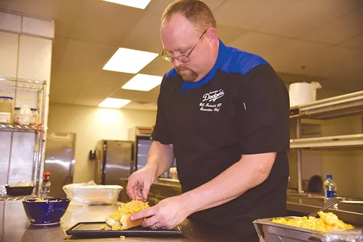 Executive chef Will Fenwick assembles a macaroni and cheese hot dog inside a kitchen at Chickasaw Bricktown Ballpark. - JACOB THREADGILL