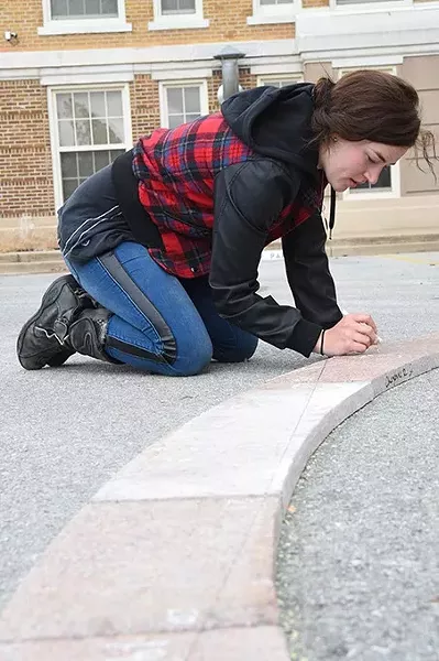 Art student Brittany Standard marks granite pieces for cutting as part of the Coming Together Park sculpture being installed on the USAO campus. mh