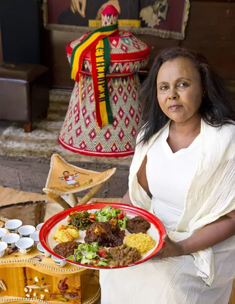Co-owner Mimi Younis holds the Queen of Sheba Mesob Dish sitting in the traditional Ethiopian dining room-from top left and clockwise potaoes and carrots, green beans and carrots, salad, beef kawatt, chickpea, lamb, salad, lentil. Chicken in the middle. All on top of Qutenga, fried Injera lightly buttered and spiced. Photo/Shannon Cornman - SHANNON CORNMAN