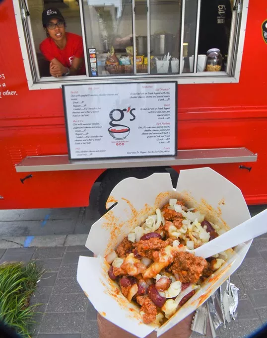 G's Chili Compan-chili mac comes in a nice cordboard to go box which you can eat on the go or close the lid and take it home. Photo of Chatoya Franklin, daughter of owner Glen Franklin, at the window of the bright red G's Chili Company food truck on location across from the Cox Convention Center recently, 8-27-15. mh