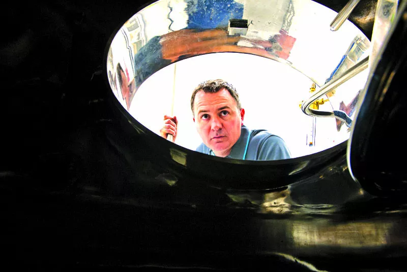 Tim Schoelen looks inside one the large stainless steel brewing vessels after a recent late night of brewing, at Mustang Brewing Company. mh