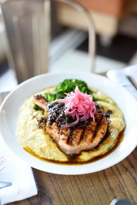 Pork chop w/ grits, broccoli, bacon jam and pickled onions at Packard's New American Kitchen, Thursday, March 31, 2016. - GARETT FISBECK