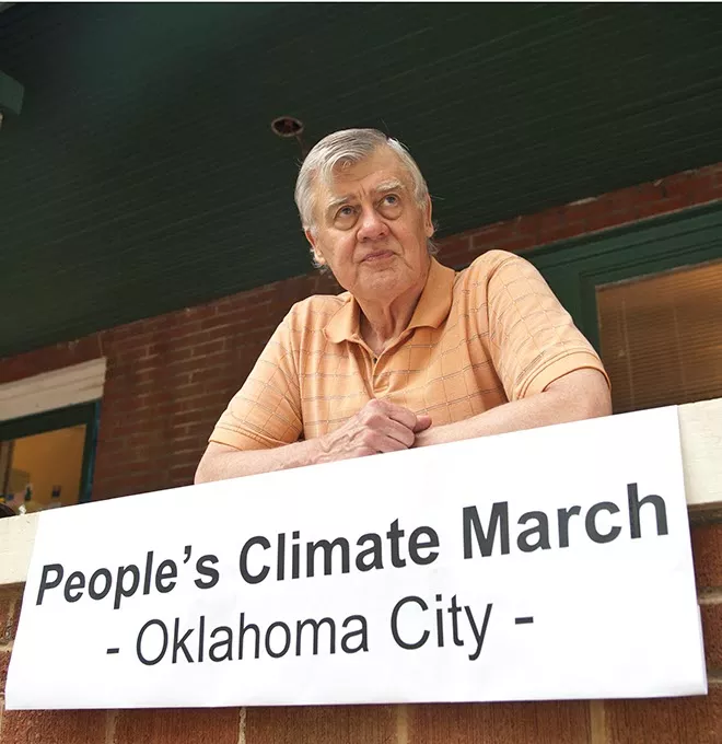 Nathaniel Batchelder, Director, on The Peace House in Oklahoma City's front porch with a banner promoting the upcoming People's Climate March. - MARK HANCOCK