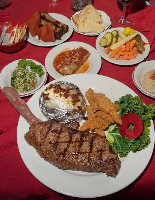 Gigantic KC Strip steak with fried catfish, baked potato, tabouleh and more sides, adorn a table at Jamil's Steakhouse. mh